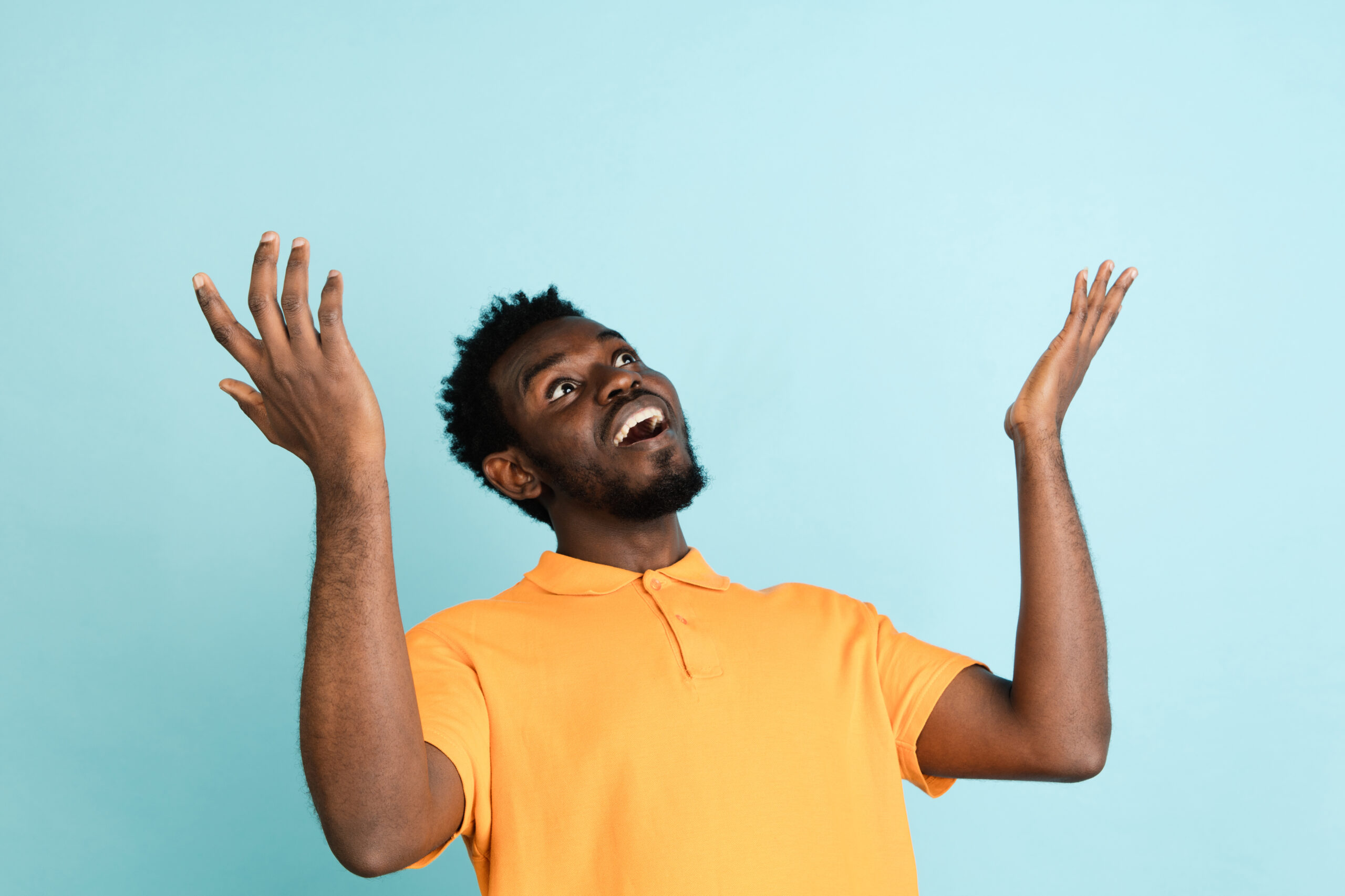 African man's portrait isolated on light blue studio background with copyspace for ad. Laughing. Male fashion model in yellow shirt. Concept of human emotions, facial expression, youth culture.
