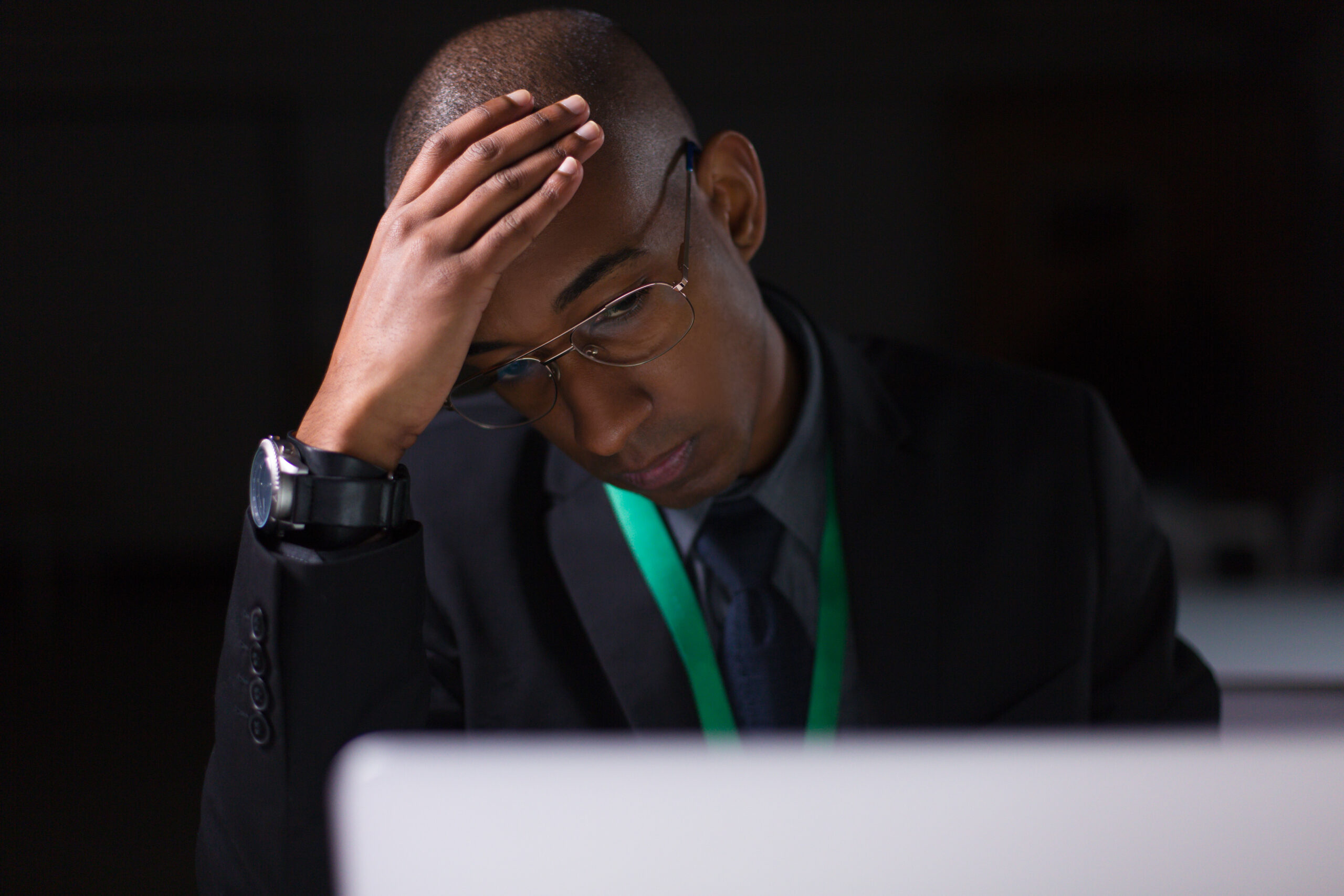 Tired manager working in office late at night. Thinking African American employee holding hand on head while sitting at table with laptop. Overwork, working late concept